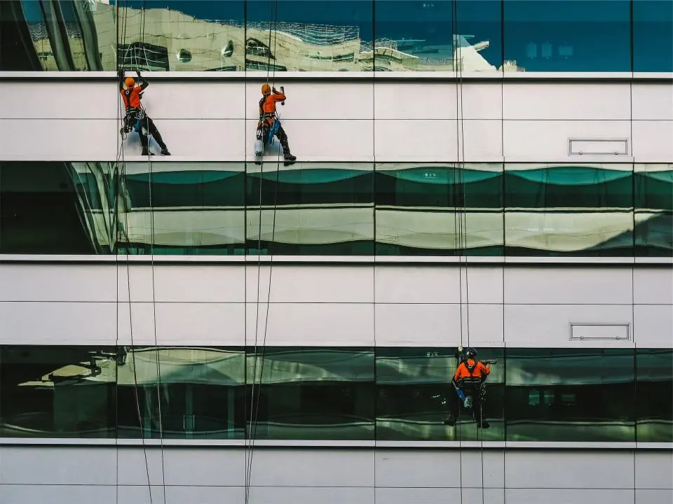 Trois cordistes nettoyant les vitres de la façade vitrée d’un grand immeuble de bureaux